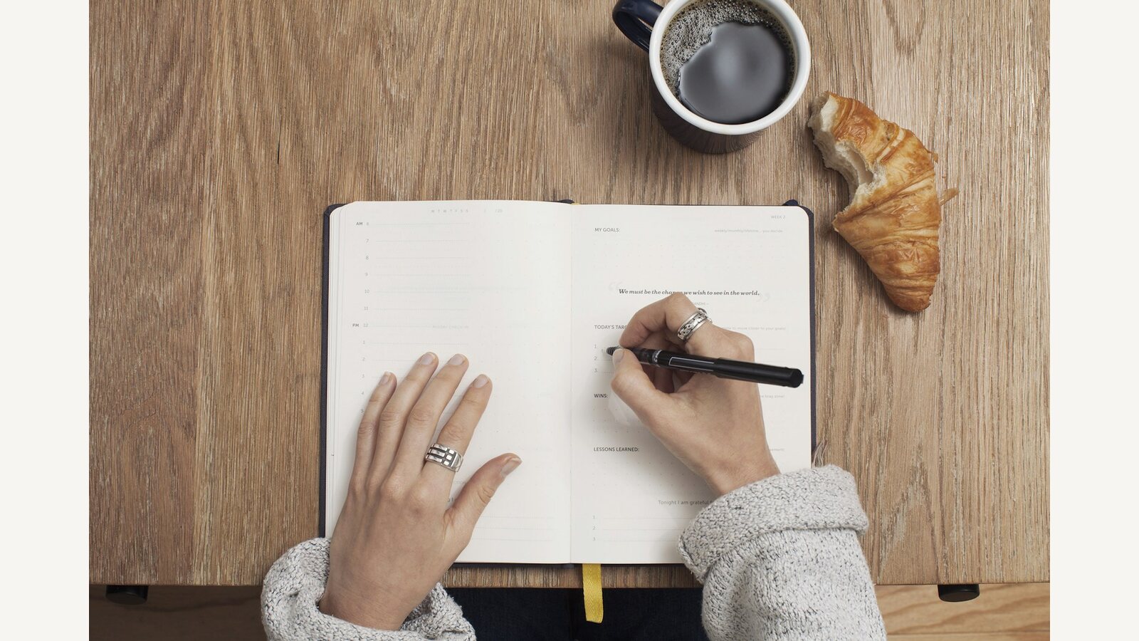 A person writing in a notebook beside a cup of coffee